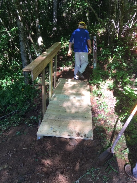 Volunteer inspecting newly constructed wooden footbridge on forest trail